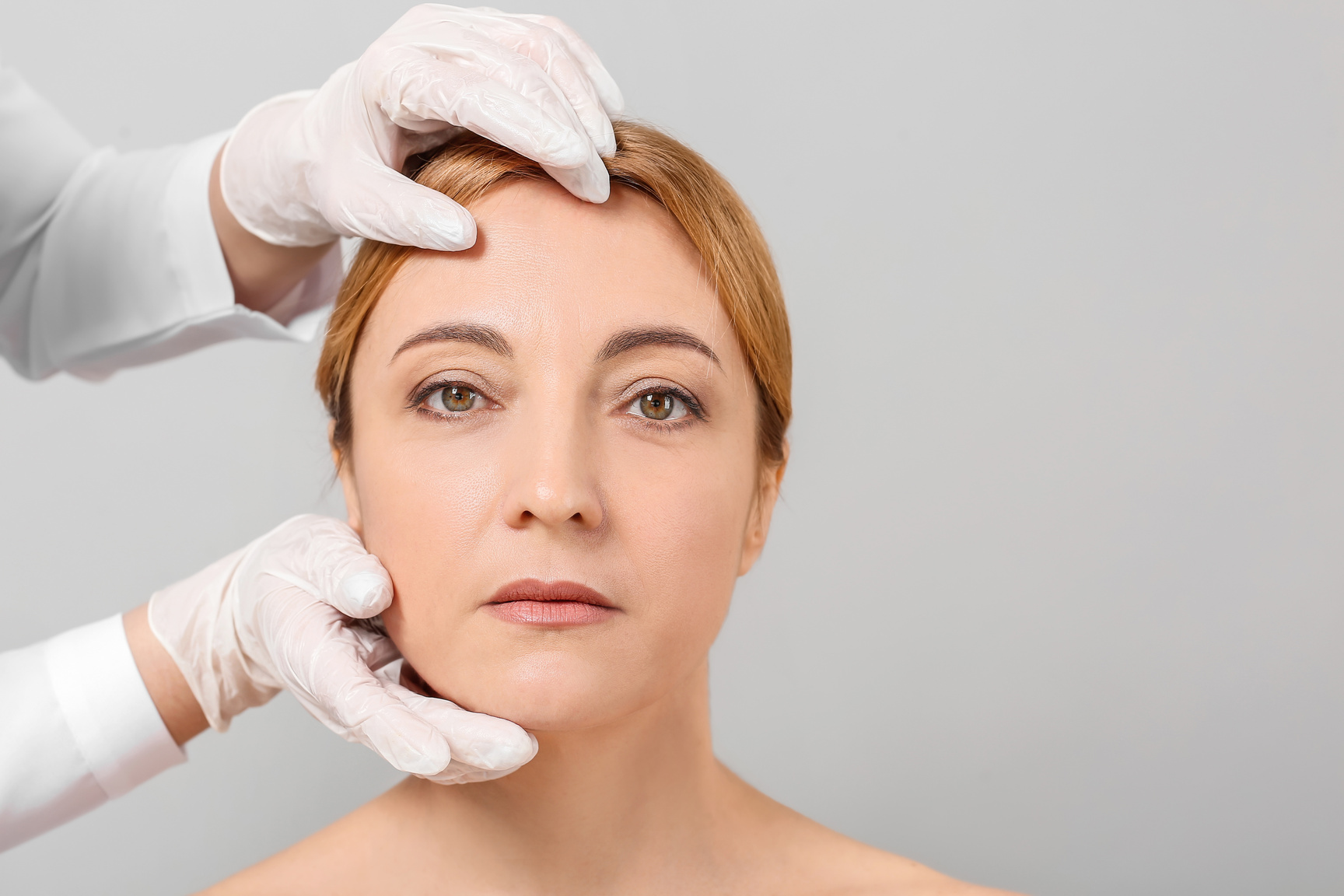 Plastic Surgeon Examines Woman Face against Grey Background